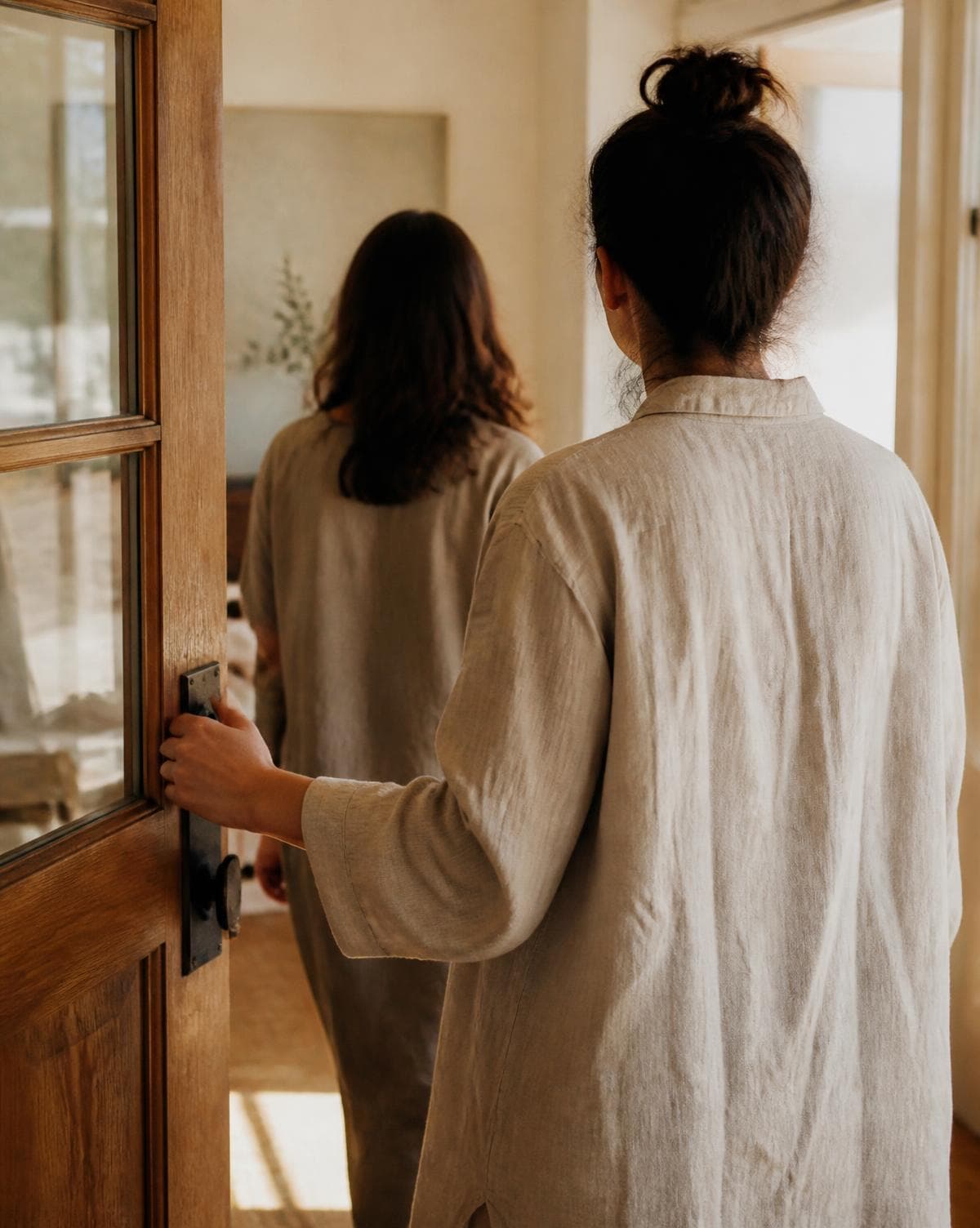 Someone holding a door open for another person entering a quiet, sunlit room